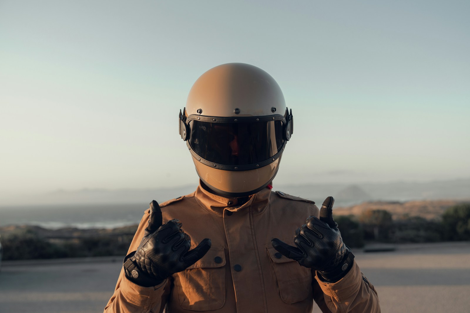 Motociclista con casco integrale chiaro e guanti in pelle al tramonto sul mare