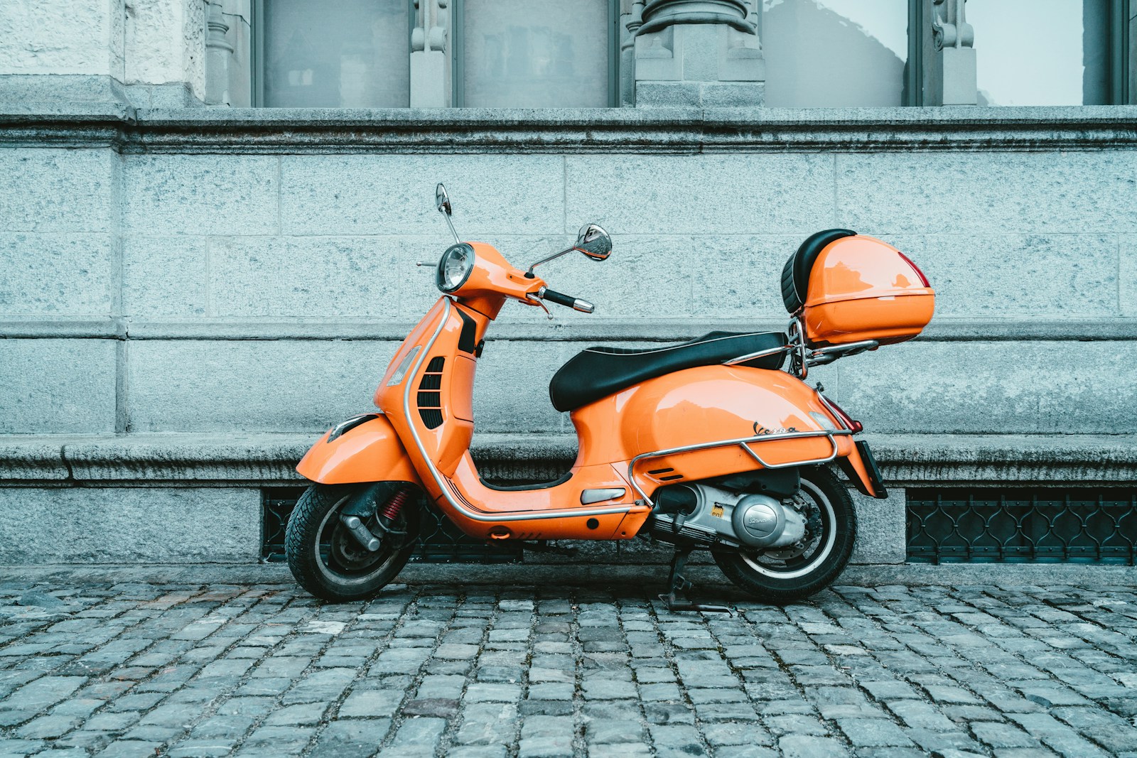 Vespa arancione parcheggiata su una strada lastricata in città