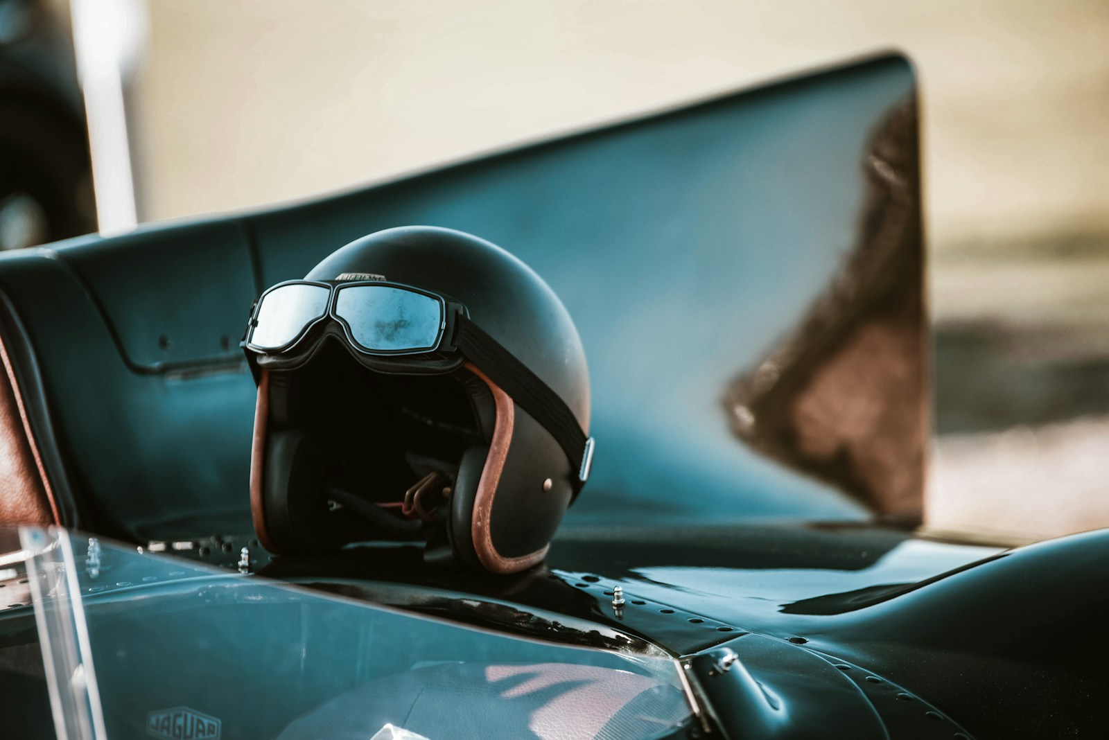 Casco jet vintage con occhiali da moto appoggiato sul cofano di un'auto d'epoca