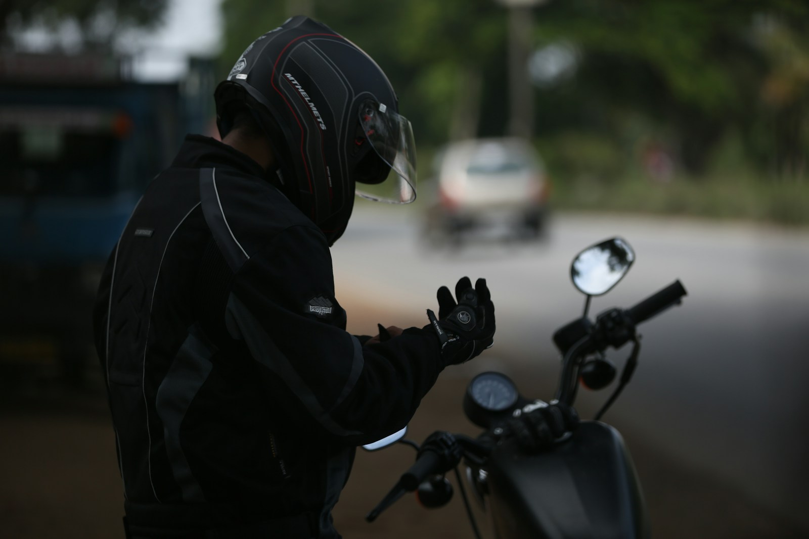 Motociclista con giacca protettiva e casco che indossa i guanti accanto alla moto