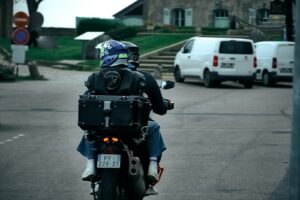 Pilota e passeggero con casco in moto con bauletto, visti da dietro