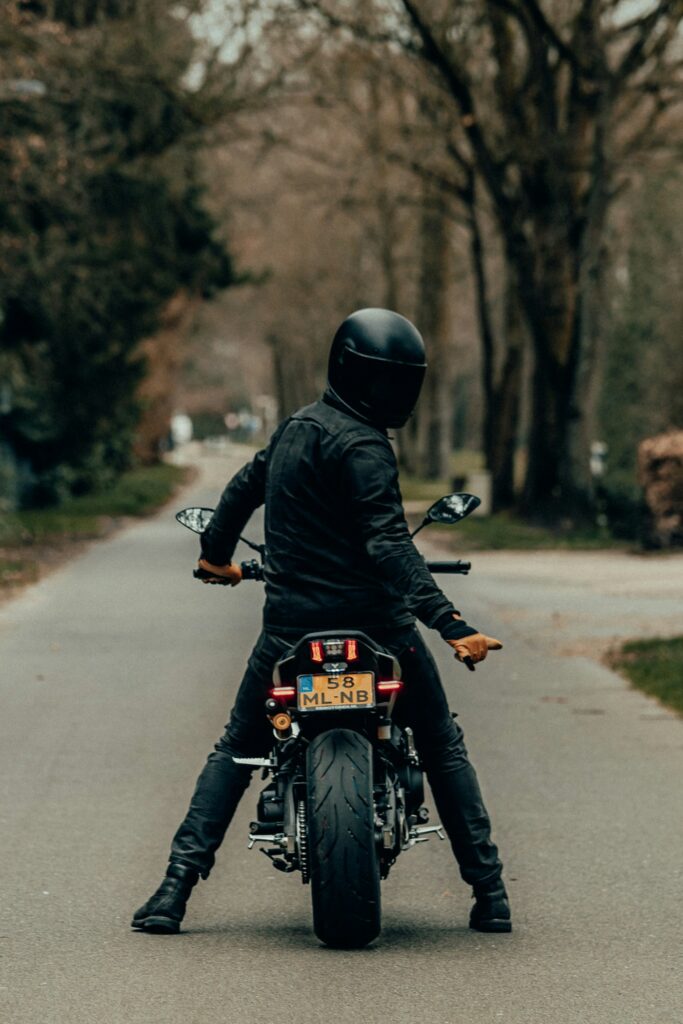 Motociclista con casco integrale fermo su una strada alberata