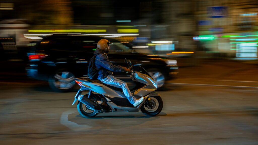 Scooterista con casco jet nel traffico cittadino di notte
